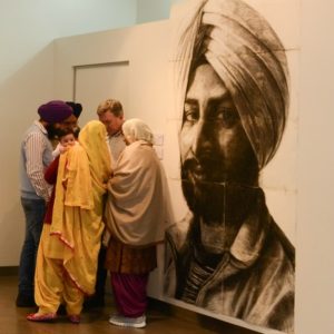 Group of people crowded around a large charcoal portrait