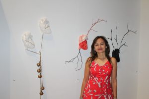 Anatomical heart shaped sculptured mounted on wall. Female artist stands next to it in a red dress.