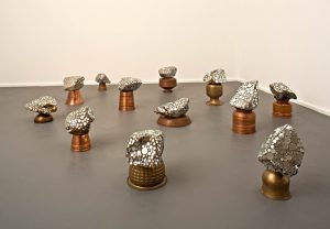 A grouping of rock like shapes with silver metal embedded in them. Each  shape is balanced on a copper pot, vase or bowl. 