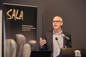 Older gentleman standing at a podium with a microphone and gesticulating as he speaks. SALA banner in the background.