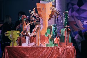 Coloured cardboard trophies roughly made each studded with different tassles or other adornments 