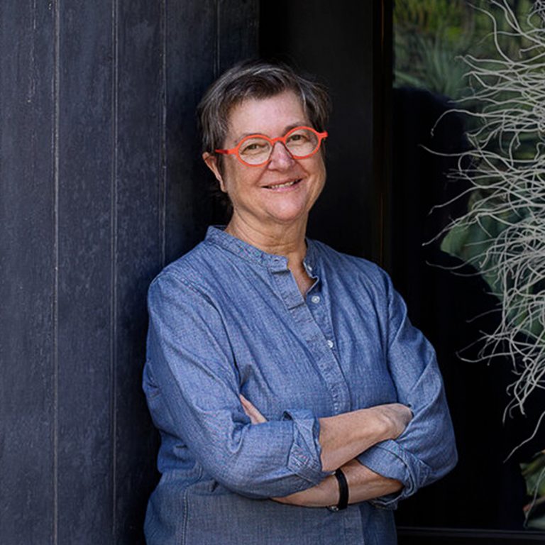 a woman with short hair and red glasses smiling, arms folded